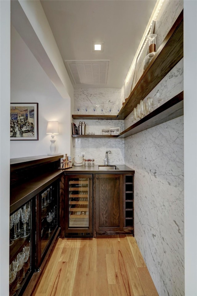 bar featuring sink, beverage cooler, and light wood-type flooring