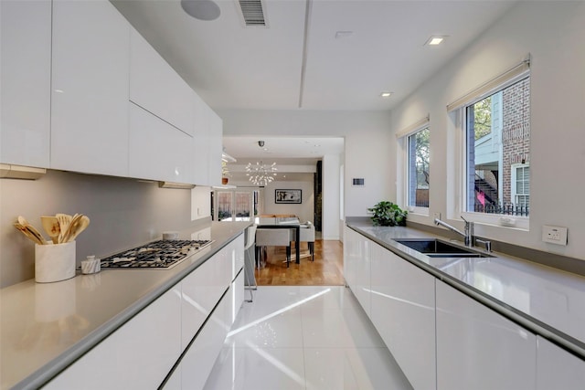 kitchen featuring sink, hanging light fixtures, light tile patterned floors, stainless steel gas stovetop, and white cabinets