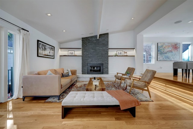 living room featuring light hardwood / wood-style flooring, a stone fireplace, and vaulted ceiling