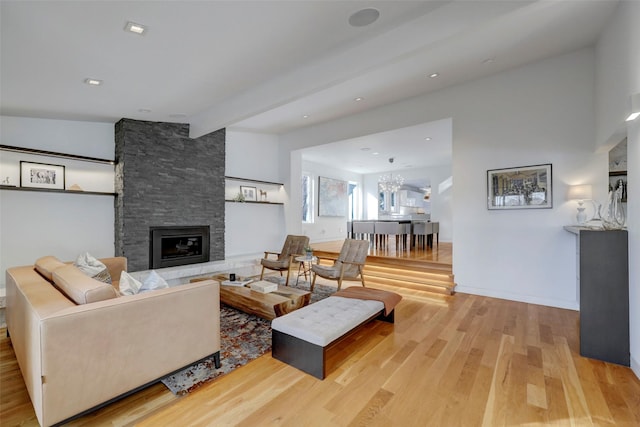 living room featuring beam ceiling, a stone fireplace, a notable chandelier, and light wood-type flooring