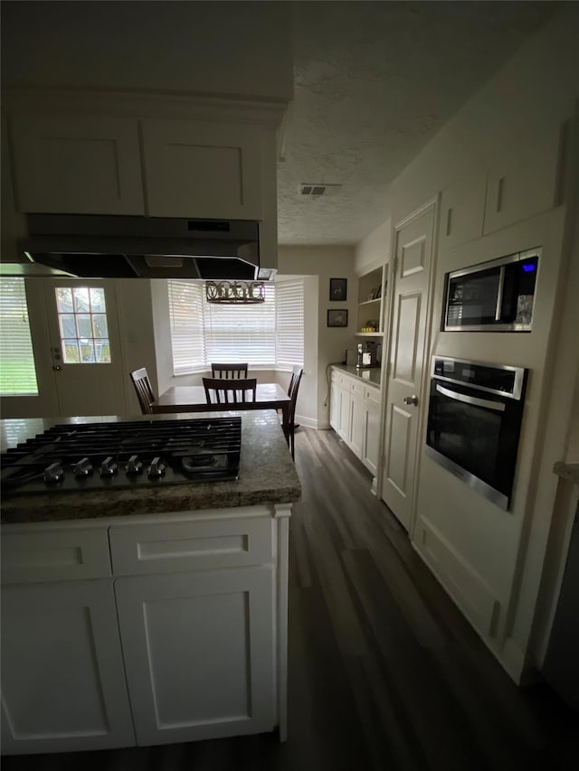 kitchen with appliances with stainless steel finishes, white cabinetry, range hood, dark stone countertops, and dark wood-type flooring