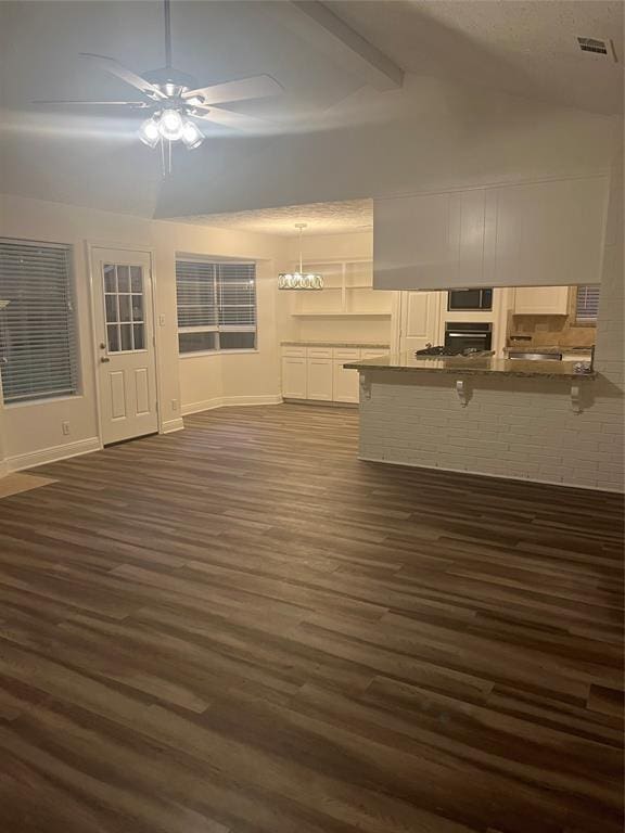 unfurnished living room with ceiling fan with notable chandelier, dark hardwood / wood-style floors, and lofted ceiling with beams