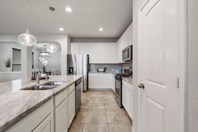 kitchen with appliances with stainless steel finishes, decorative light fixtures, sink, white cabinets, and light stone counters