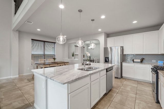 kitchen with appliances with stainless steel finishes, a kitchen island with sink, hanging light fixtures, white cabinetry, and light stone counters