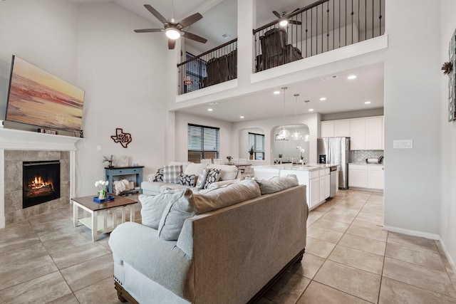 tiled living room with a tiled fireplace, a towering ceiling, and ceiling fan