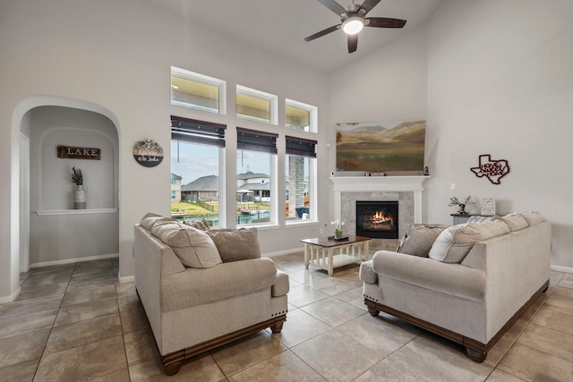 living room featuring ceiling fan, tile patterned floors, a tiled fireplace, and high vaulted ceiling