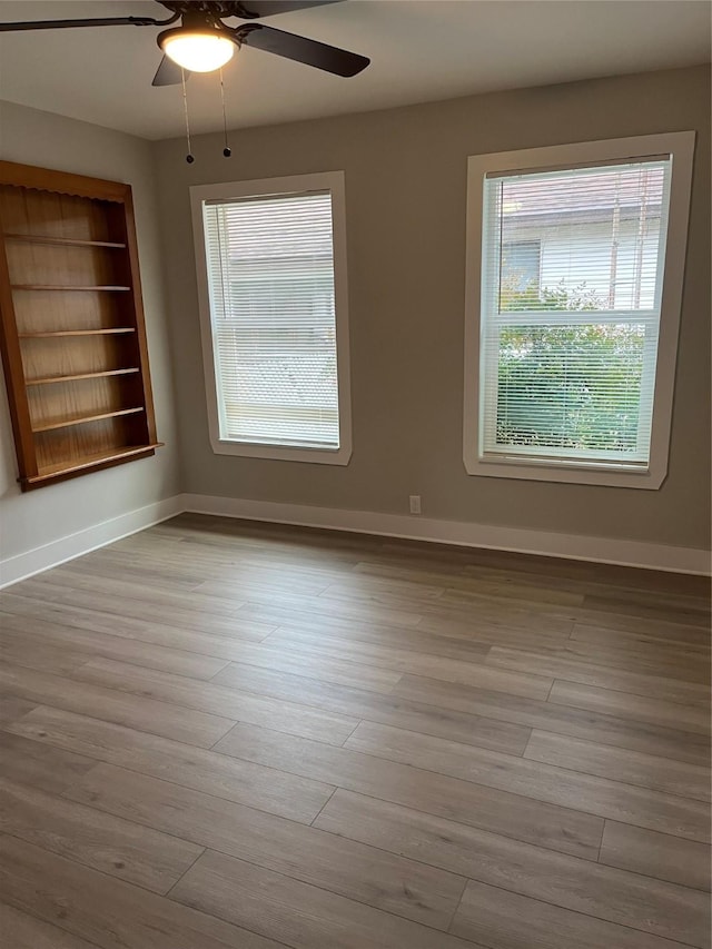 empty room featuring built in features, ceiling fan, and light wood-type flooring