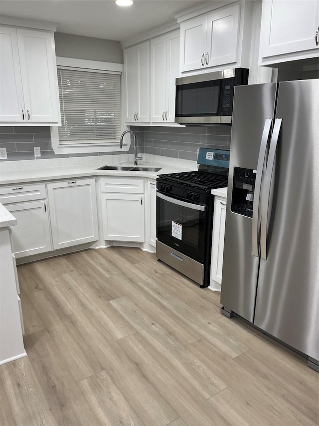 kitchen featuring sink, appliances with stainless steel finishes, backsplash, white cabinets, and light wood-type flooring