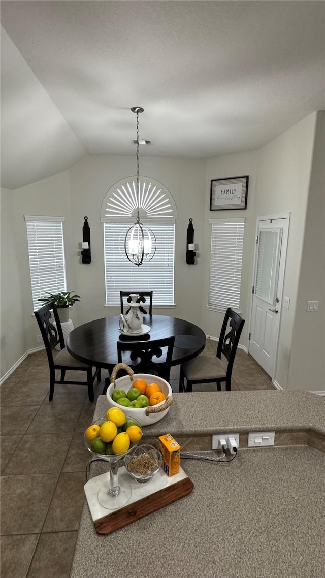 dining space featuring dark tile patterned floors, lofted ceiling, and a chandelier