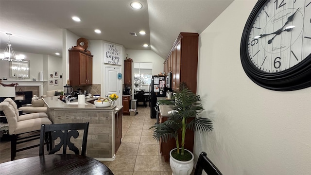 kitchen with pendant lighting, light tile patterned floors, a fireplace, an inviting chandelier, and lofted ceiling