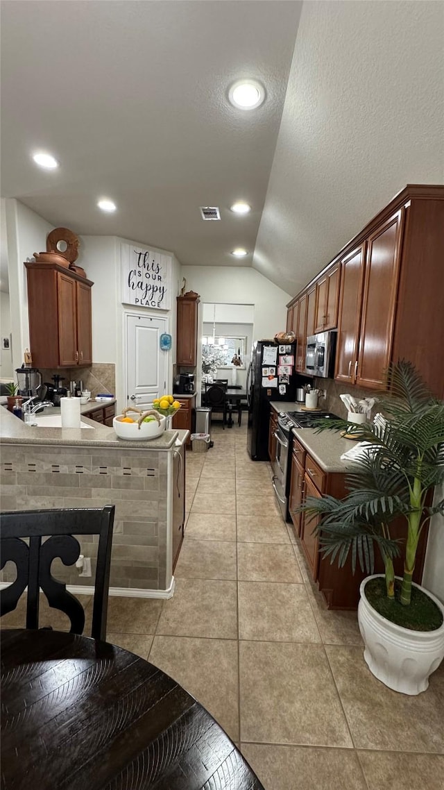 kitchen featuring light tile patterned flooring, appliances with stainless steel finishes, decorative backsplash, and lofted ceiling