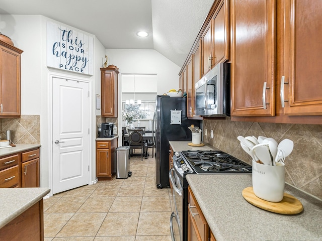 kitchen featuring light tile patterned floors, backsplash, vaulted ceiling, and stainless steel appliances