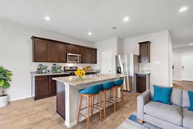 kitchen with dark brown cabinets, appliances with stainless steel finishes, sink, an island with sink, and light hardwood / wood-style floors