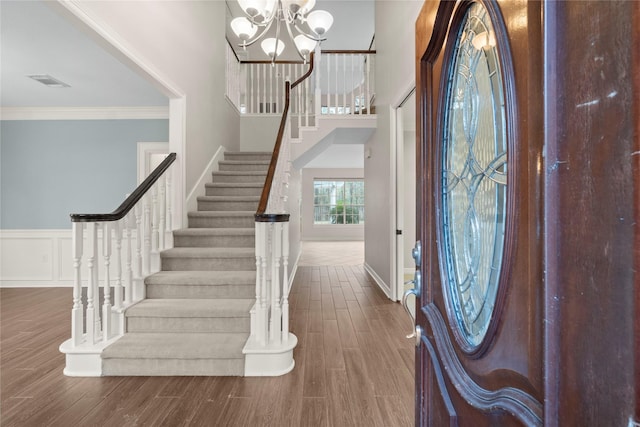 foyer entrance featuring an inviting chandelier, hardwood / wood-style floors, a towering ceiling, and ornamental molding