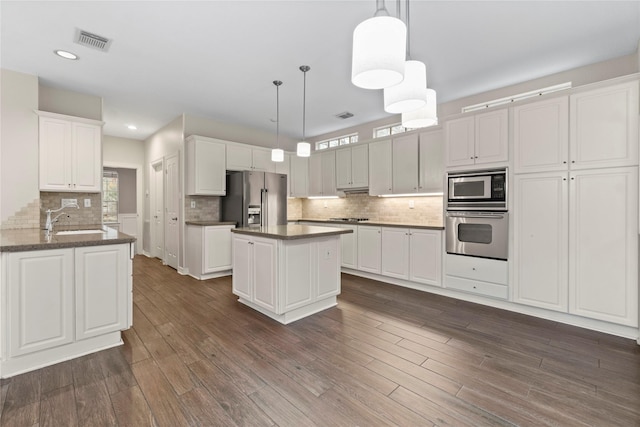 kitchen with sink, appliances with stainless steel finishes, kitchen peninsula, pendant lighting, and white cabinets