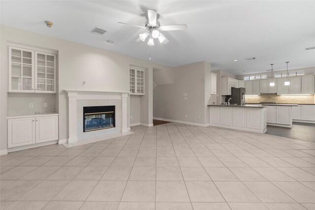 unfurnished living room featuring a tiled fireplace, light tile patterned floors, and ceiling fan