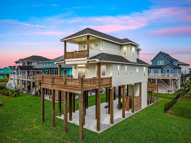 back house at dusk with a balcony, a wooden deck, a patio area, and a yard