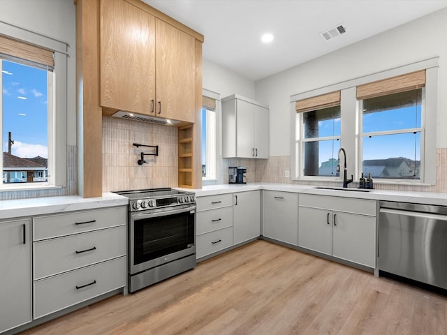 kitchen featuring appliances with stainless steel finishes, sink, backsplash, extractor fan, and light wood-type flooring