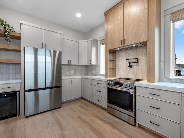 kitchen with a wealth of natural light, appliances with stainless steel finishes, wall chimney exhaust hood, decorative backsplash, and light hardwood / wood-style floors