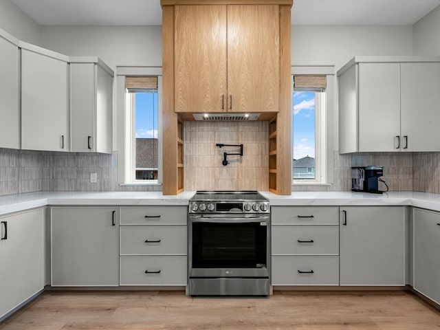 kitchen with light wood-type flooring, exhaust hood, tasteful backsplash, and stainless steel electric stove