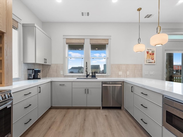 kitchen with light stone countertops, appliances with stainless steel finishes, decorative light fixtures, sink, and backsplash