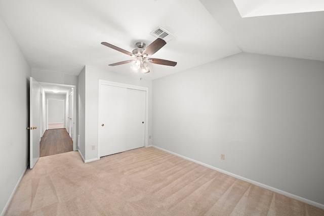 unfurnished bedroom featuring light carpet, a closet, vaulted ceiling, and ceiling fan