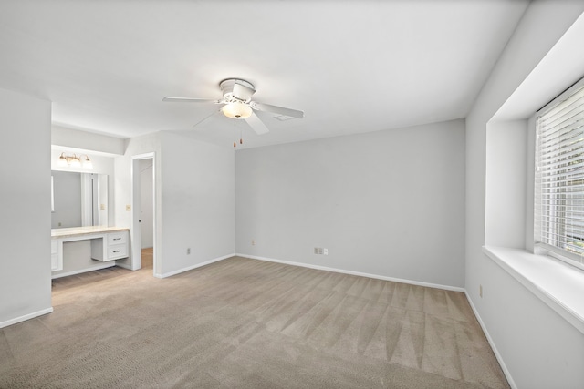 unfurnished bedroom featuring light colored carpet, ensuite bath, ceiling fan, and built in desk