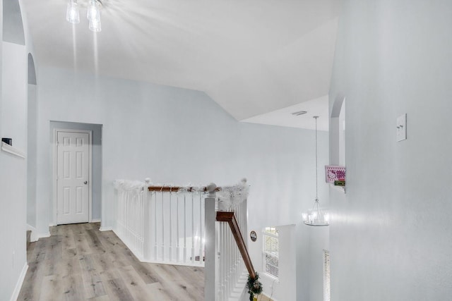 hall with an inviting chandelier, light hardwood / wood-style floors, and vaulted ceiling