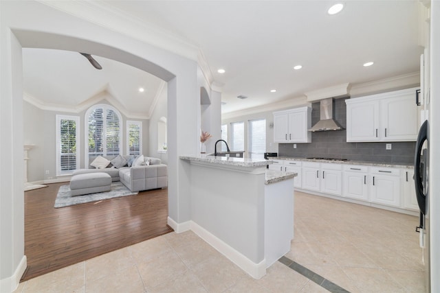 kitchen featuring wall chimney range hood, gas cooktop, white cabinetry, and light tile patterned flooring