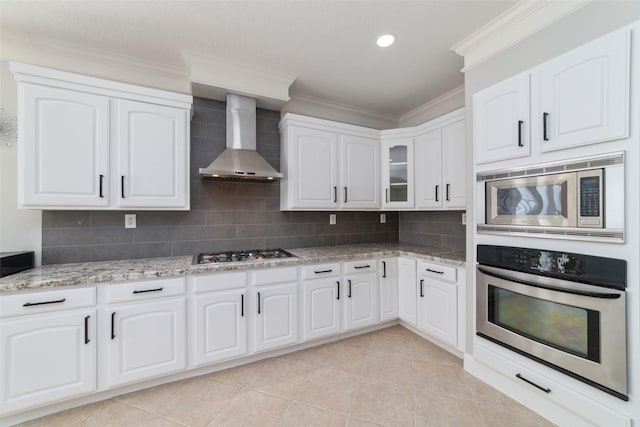 kitchen featuring wall chimney range hood, white cabinets, stainless steel appliances, and tasteful backsplash