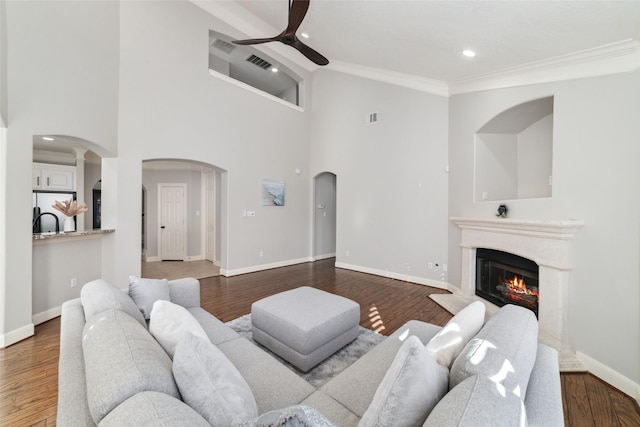 living room with ceiling fan, a high ceiling, wood-type flooring, and ornamental molding