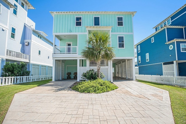 coastal home featuring an attached garage, fence, board and batten siding, and decorative driveway