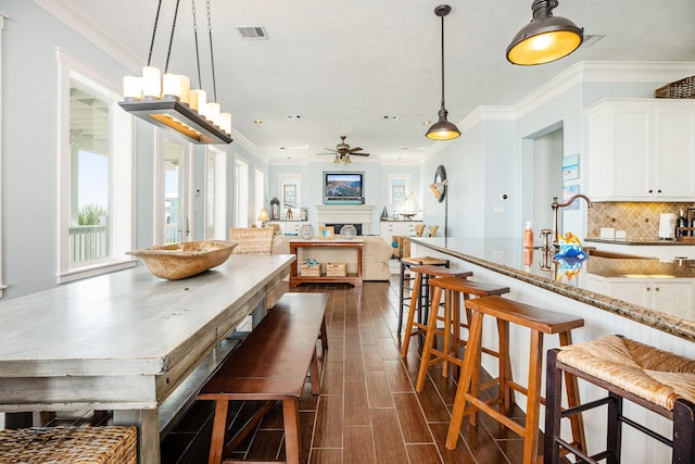 dining space with ornamental molding, visible vents, wood finish floors, and ceiling fan