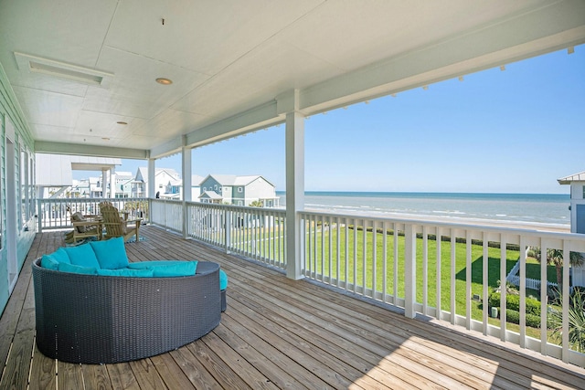 deck with an outdoor living space, a water view, a yard, and a view of the beach