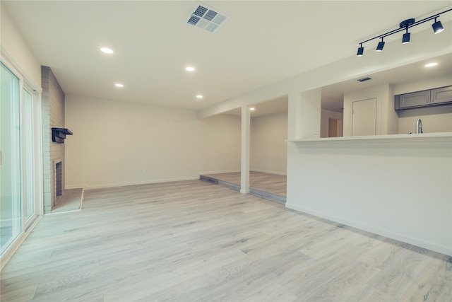 interior space with light wood-type flooring, track lighting, a brick fireplace, and sink