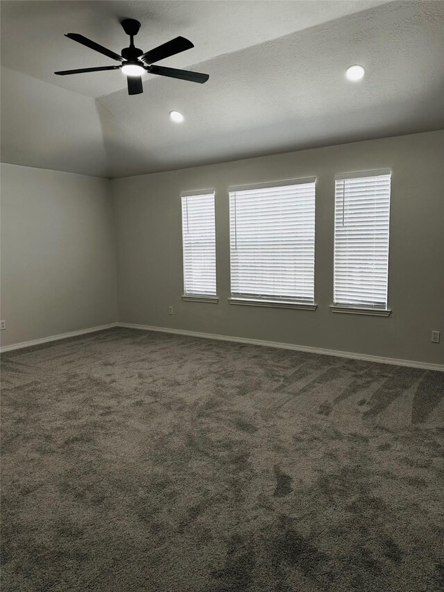 unfurnished room with ceiling fan, dark colored carpet, plenty of natural light, and lofted ceiling