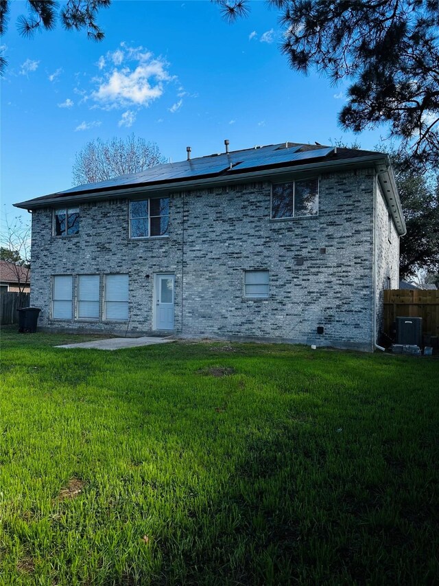 rear view of property featuring cooling unit, a lawn, and solar panels