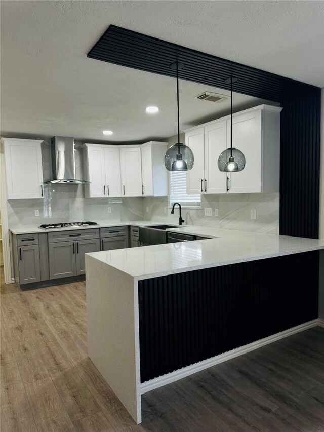 kitchen featuring light hardwood / wood-style floors, sink, kitchen peninsula, pendant lighting, and wall chimney exhaust hood