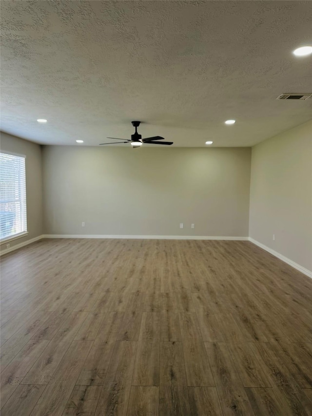 empty room with ceiling fan, wood-type flooring, and a textured ceiling