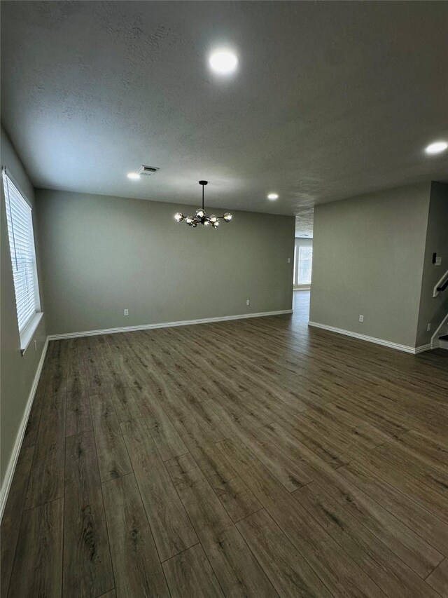 empty room featuring a notable chandelier, dark hardwood / wood-style floors, and a textured ceiling