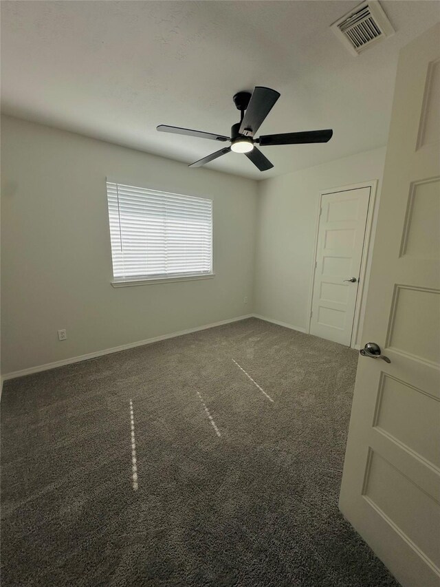 spare room featuring ceiling fan and dark colored carpet