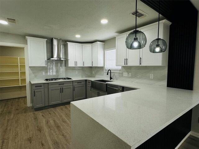 kitchen with wall chimney exhaust hood, white cabinetry, kitchen peninsula, and hanging light fixtures