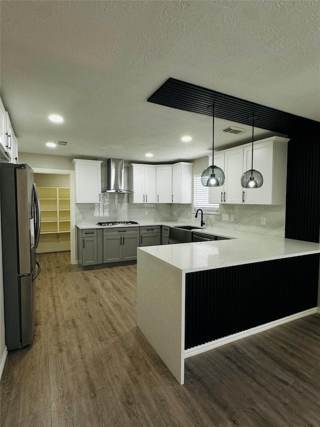 kitchen with tasteful backsplash, decorative light fixtures, kitchen peninsula, wall chimney exhaust hood, and stainless steel fridge