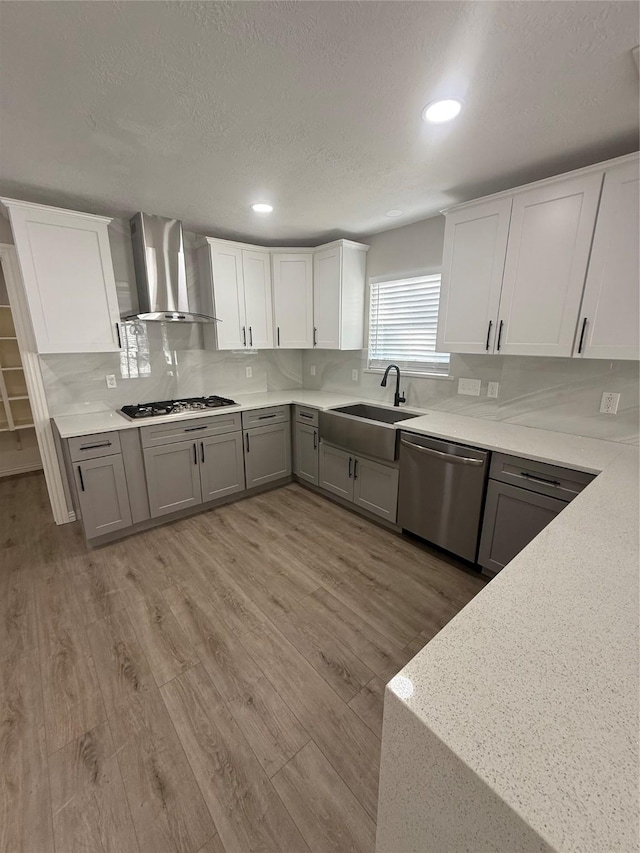 kitchen featuring light wood-style floors, appliances with stainless steel finishes, wall chimney exhaust hood, and gray cabinetry