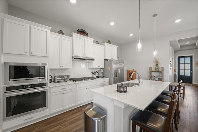 kitchen with appliances with stainless steel finishes, white cabinetry, hanging light fixtures, a kitchen island with sink, and sink