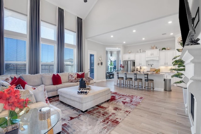 living room featuring crown molding, sink, high vaulted ceiling, and light hardwood / wood-style flooring