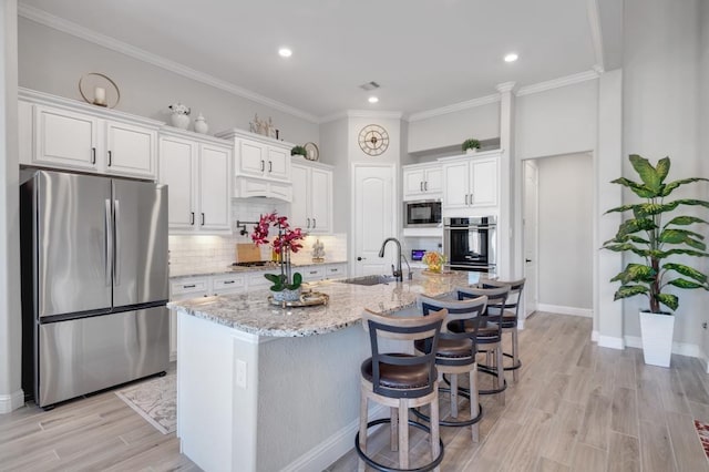 kitchen with appliances with stainless steel finishes, a breakfast bar, white cabinets, a kitchen island with sink, and light stone counters