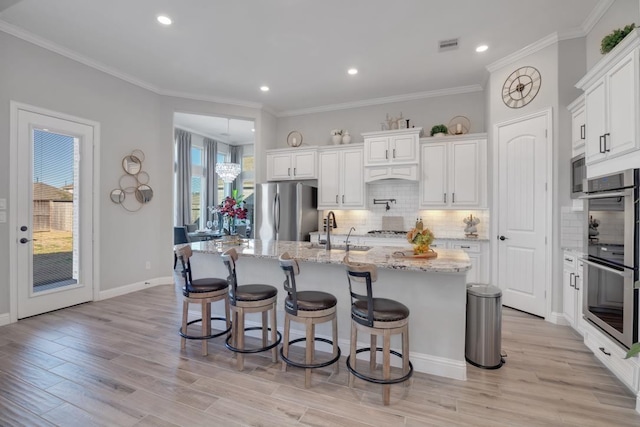 kitchen with sink, appliances with stainless steel finishes, an island with sink, light stone countertops, and white cabinets