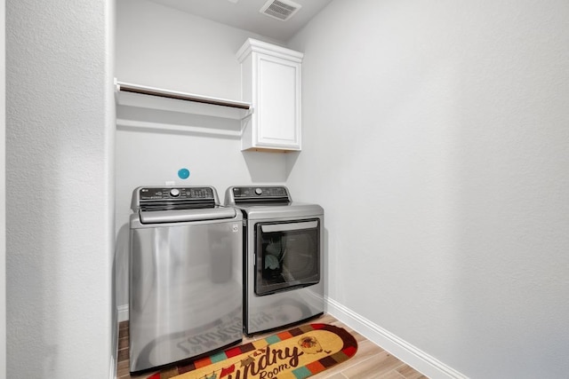 clothes washing area featuring cabinets, washing machine and dryer, and light hardwood / wood-style flooring