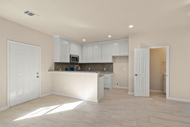 kitchen featuring white cabinets, kitchen peninsula, decorative backsplash, and sink